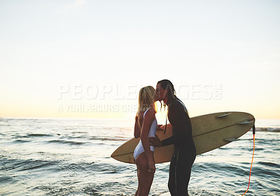 Buy stock photo Cropped shot of an affectionate young couple with a surfboard kissing on the beach at sunset