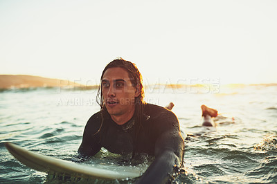 Buy stock photo Shot of a young man paddling on a surfboard in the sea