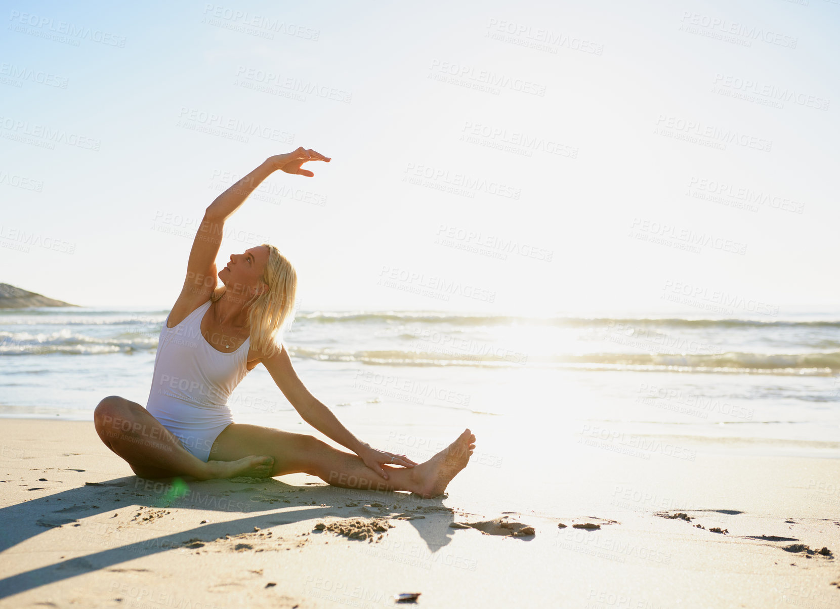 Buy stock photo Full length shot of an attractive young woman doing a yoga stretch early in the morning on the beach