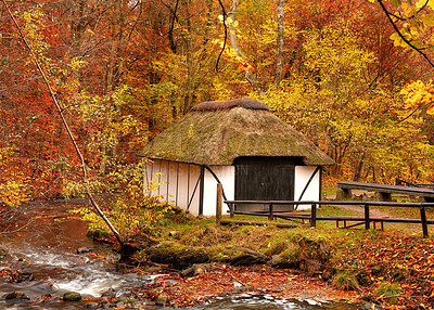 Buy stock photo A cottage in the countryside in autumn landscape beside a river in Europe. Peaceful and quiet nature scene of rustic barn or boathouse near calm water and changing season of red and yellow leaves