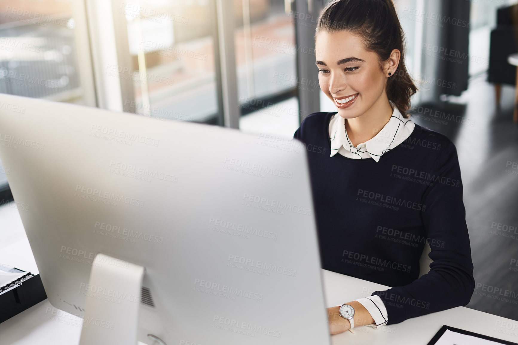 Buy stock photo Shot of an attractive young businesswoman sitting at her desk and smiling while using her computer in a modern office
