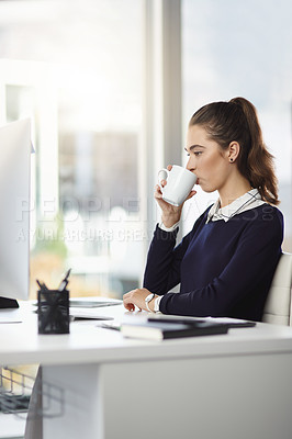 Buy stock photo Shot of an attractive young businesswoman sitting at her desk and enjoying a cup of coffee in a modern office