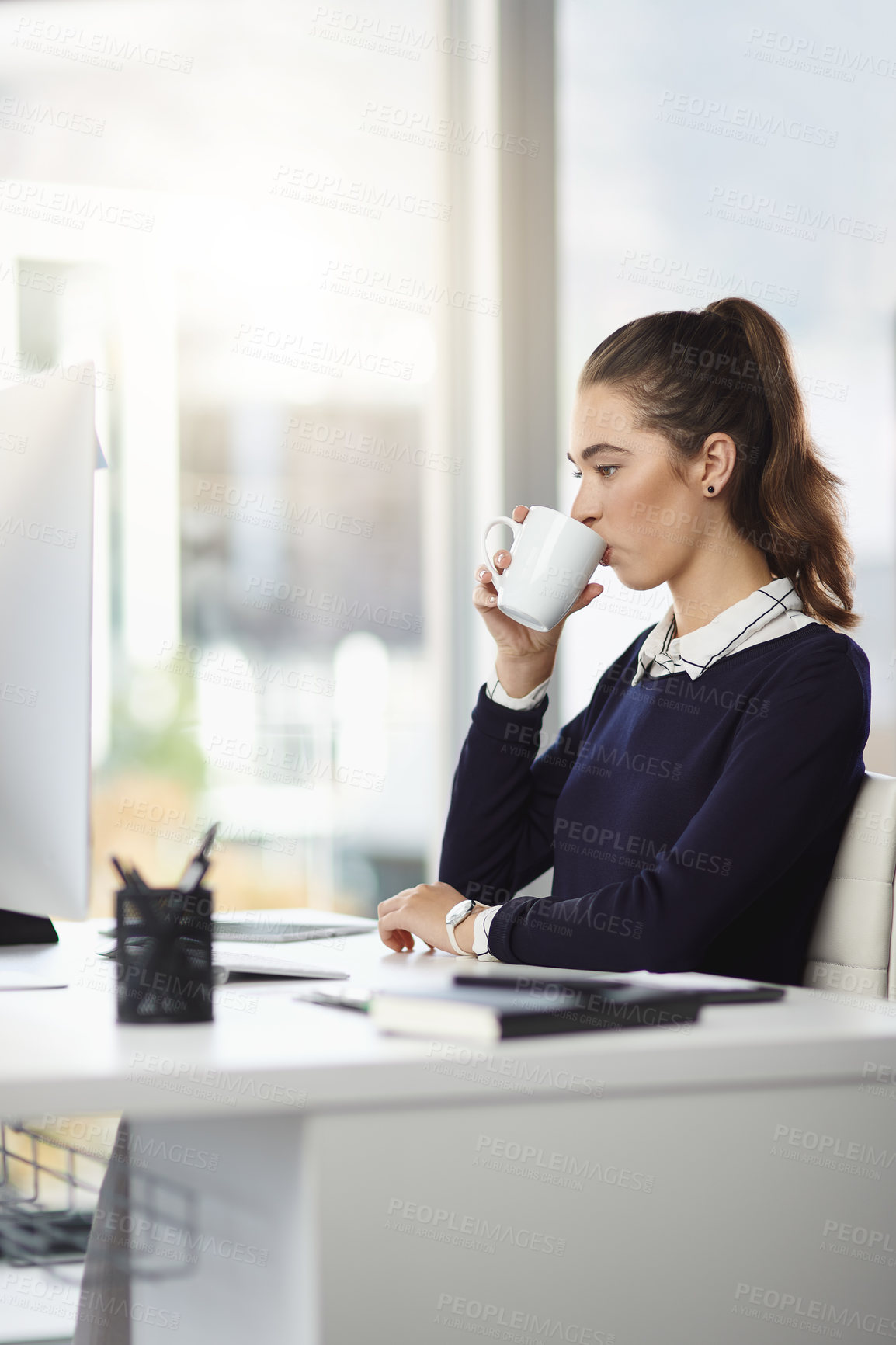 Buy stock photo Shot of an attractive young businesswoman sitting at her desk and enjoying a cup of coffee in a modern office