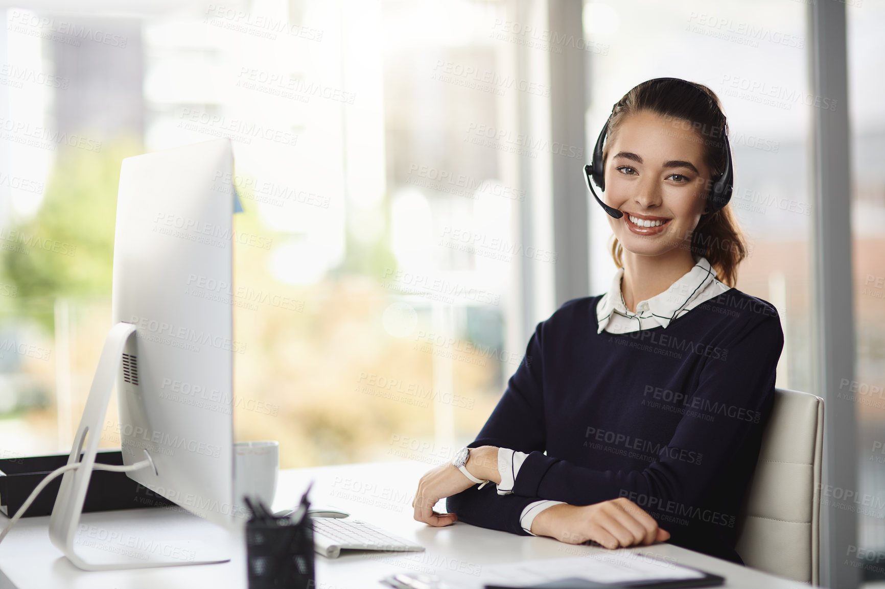 Buy stock photo Portrait of a smiling attractive young businesswoman wearing a headset and sitting at her desk in a modern office