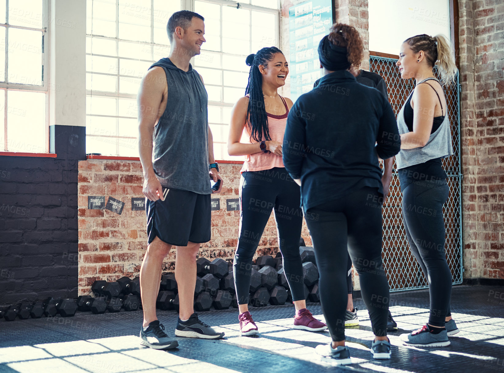 Buy stock photo Shot of a cheerful young group of people standing in a circle and having a conversation before a workout in a gym