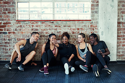 Buy stock photo Shot of a cheerful young group of people sitting down on the floor and taking a self portrait together in a gym