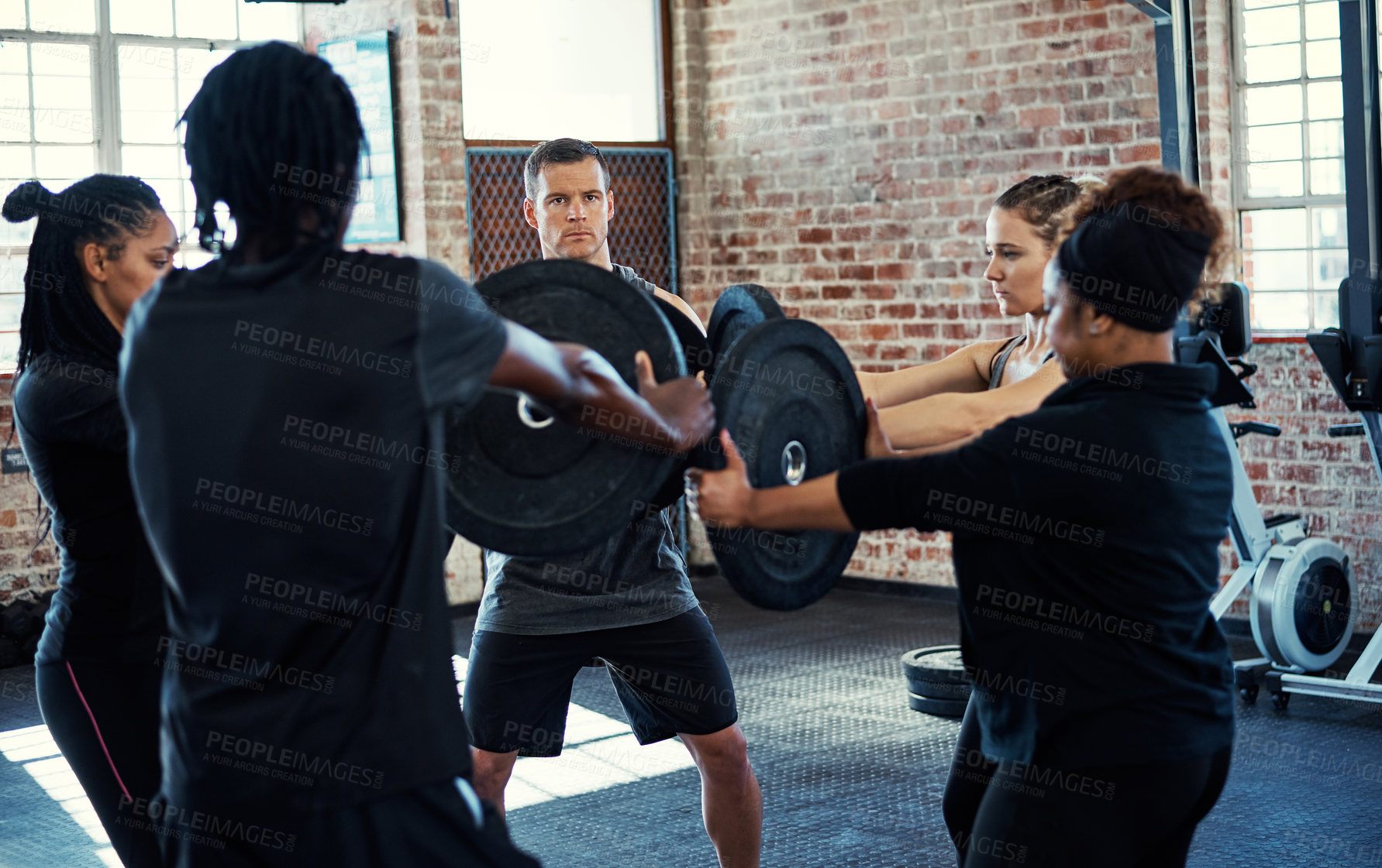 Buy stock photo Shot of a focused young group of people standing in a circle with their arms stretched out holding a weight in a gym