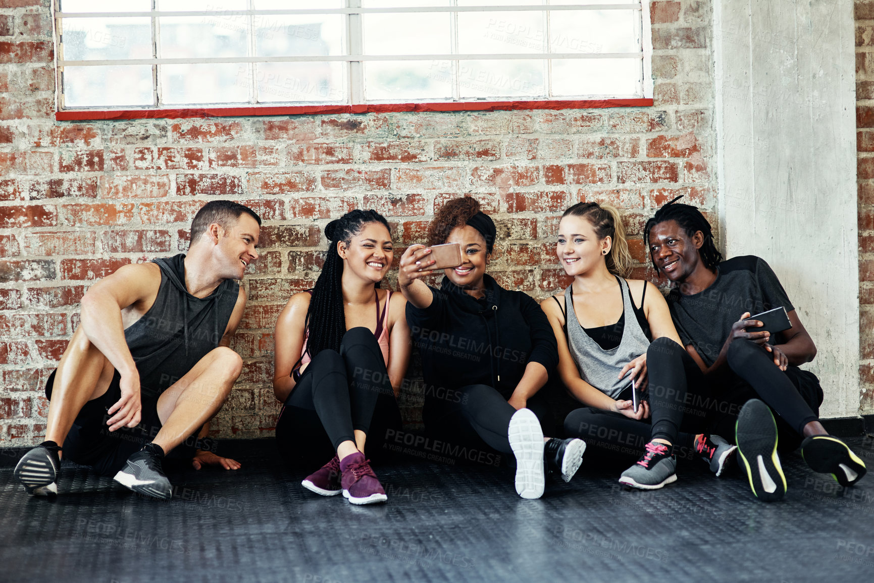 Buy stock photo Shot of a cheerful young group of people sitting down on the floor and taking a self portrait together in a gym