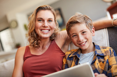 Buy stock photo Shot of an adorable little boy using a digital tablet with his mother on the sofa at home