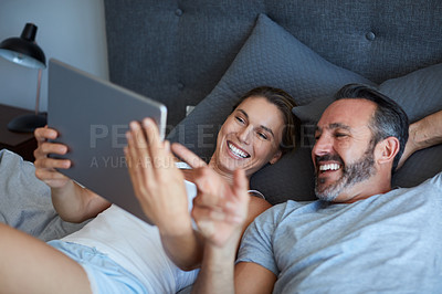 Buy stock photo High angle shot of an affectionate couple using a digital tablet while lying in bed together in the morning