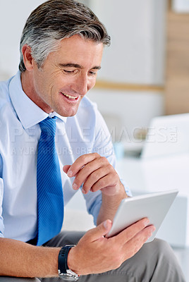Buy stock photo Shot of a confident mature businessman sitting on a sofa indoors while working on a tablet