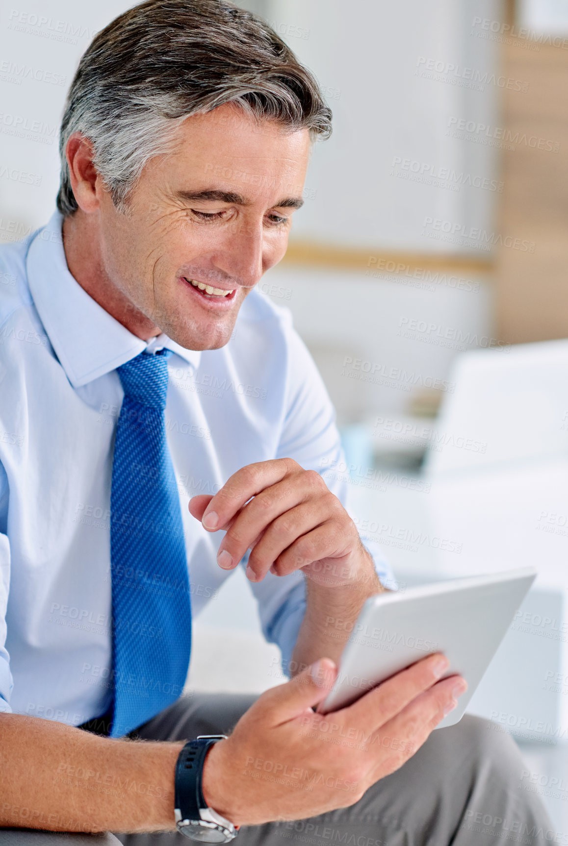 Buy stock photo Shot of a confident mature businessman sitting on a sofa indoors while working on a tablet
