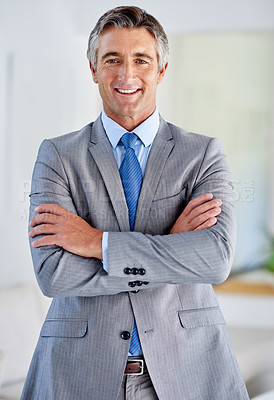 Buy stock photo Portrait of a confident mature businessman wearing a suit and standing indoors with his arms crossed