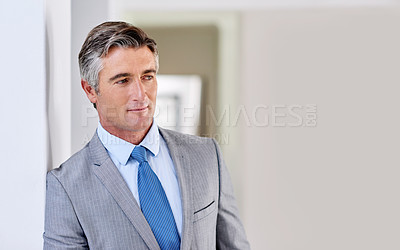 Buy stock photo Shot of a confident mature businessman wearing a suit and looking away while leaning against a wall indoors