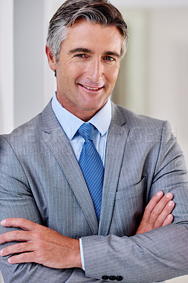 Buy stock photo Portrait of a confident mature businessman wearing a suit and standing indoors with his arms crossed
