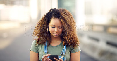 Buy stock photo Cropped shot of an attractive young woman standing outdoors and looking down while using her cellphone