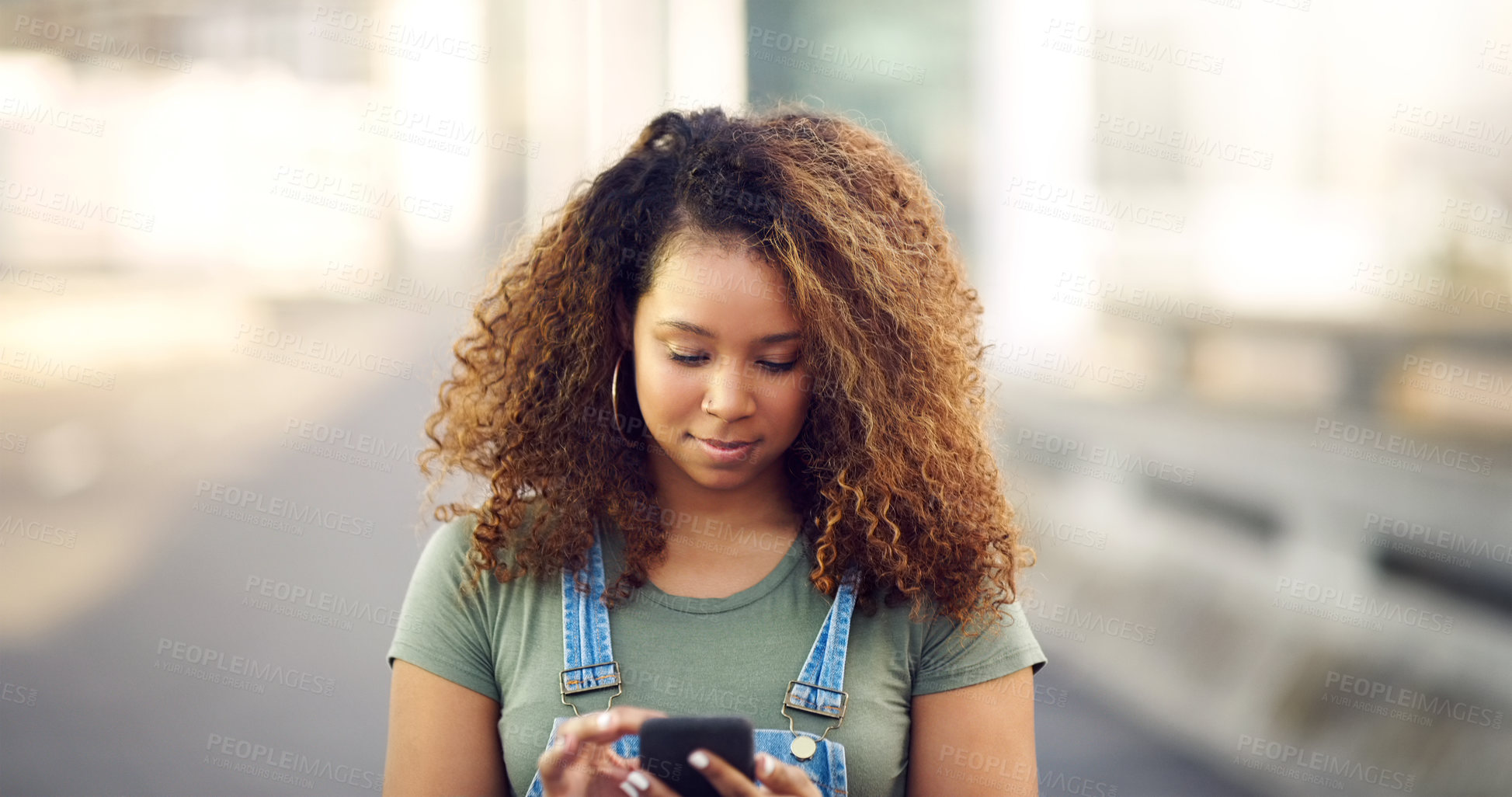 Buy stock photo Cropped shot of an attractive young woman standing outdoors and looking down while using her cellphone