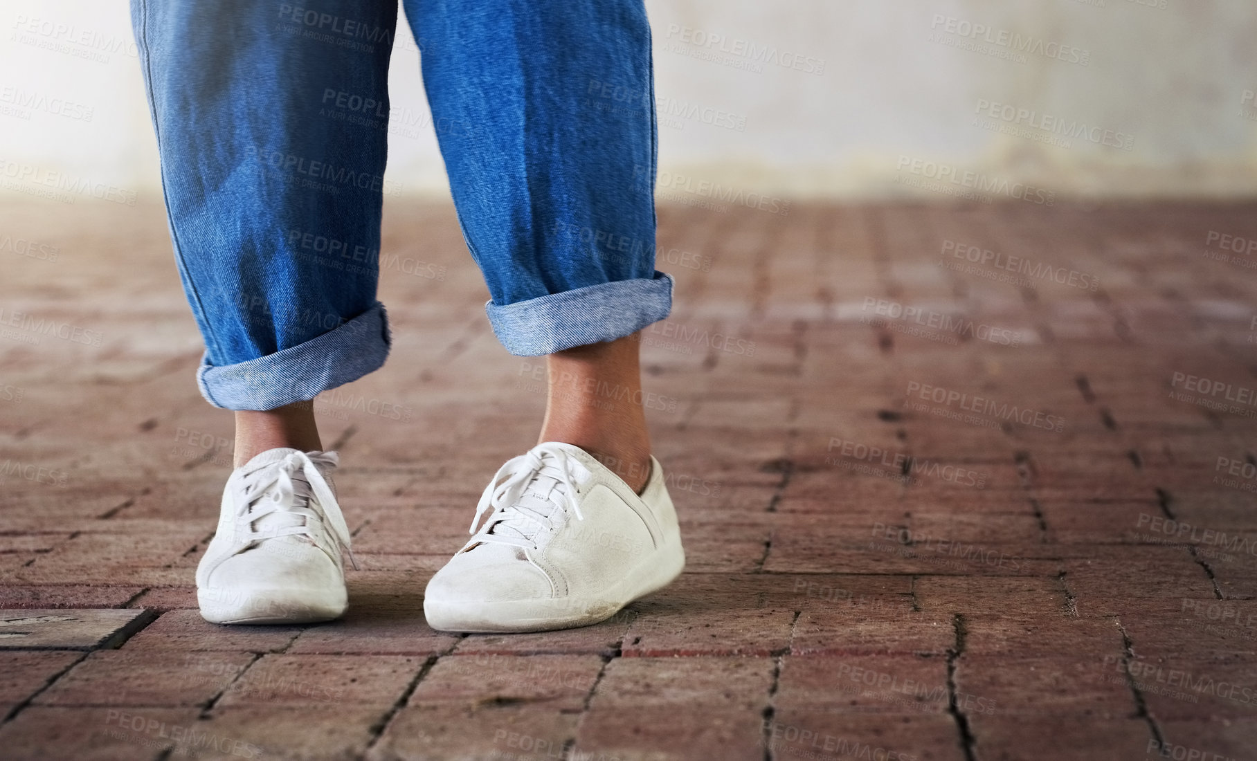 Buy stock photo Cropped shot of an unrecognizable person standing on a brick floor while wearing white sneakers and blue jeans