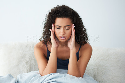 Buy stock photo Shot of an attractive young woman suffering from a headache and rubbing her head while in bed