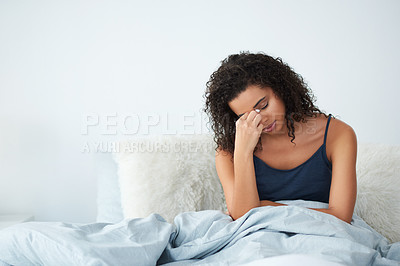 Buy stock photo Shot of an attractive young woman suffering from a headache and sitting in bed pinching her nose in the morning
