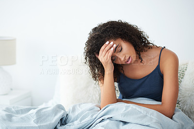 Buy stock photo Shot of an attractive young woman suffering from a headache and rubbing her forehead while in bed