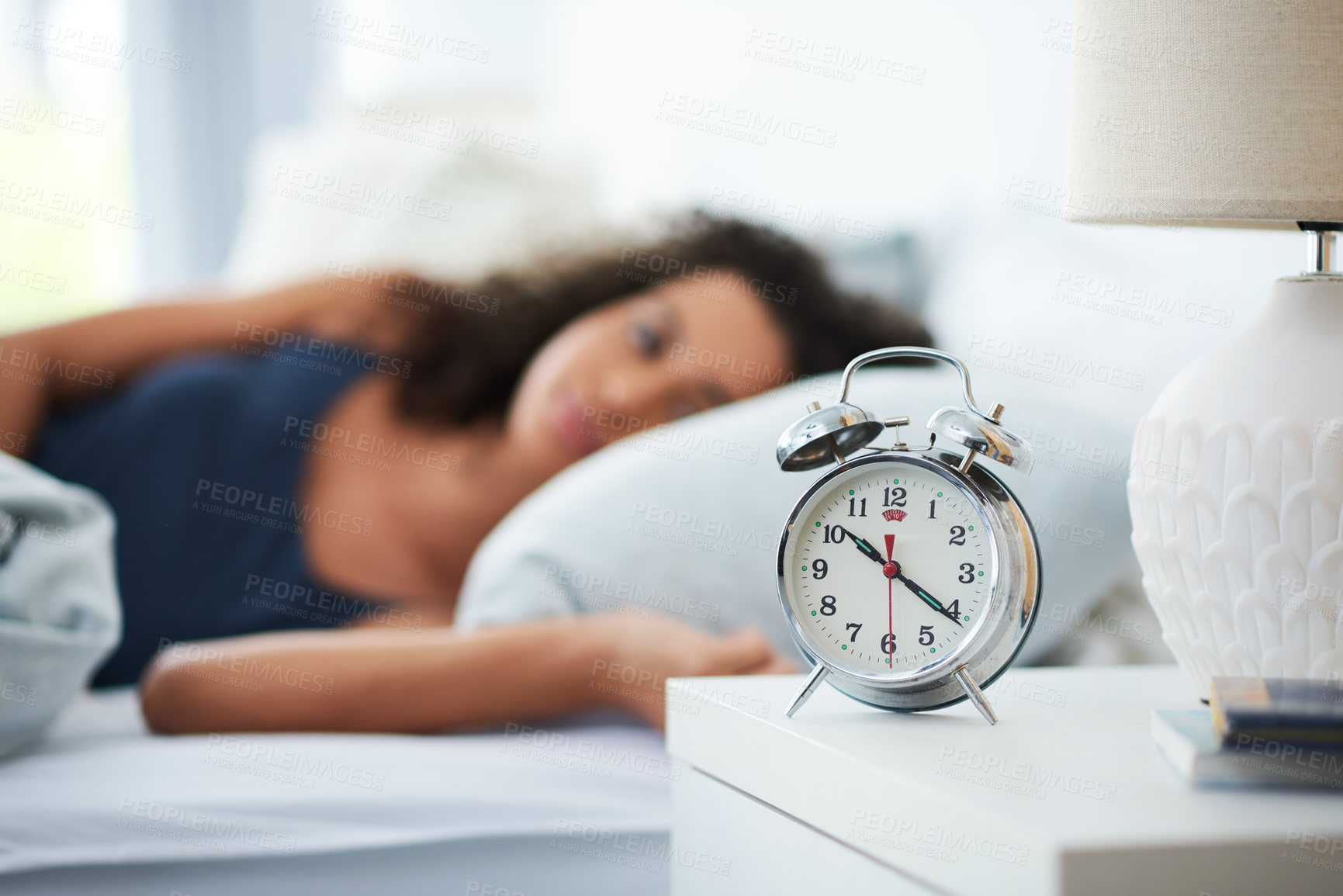 Buy stock photo Shot of an attractive young woman laying in bed with an alarm clock on her bedside table