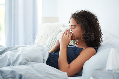 Buy stock photo Shot of an attractive young woman feeling sick and blowing her nose while in bed in the morning