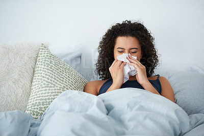 Buy stock photo Shot of an attractive young woman feeling sick and blowing her nose while in bed in the morning