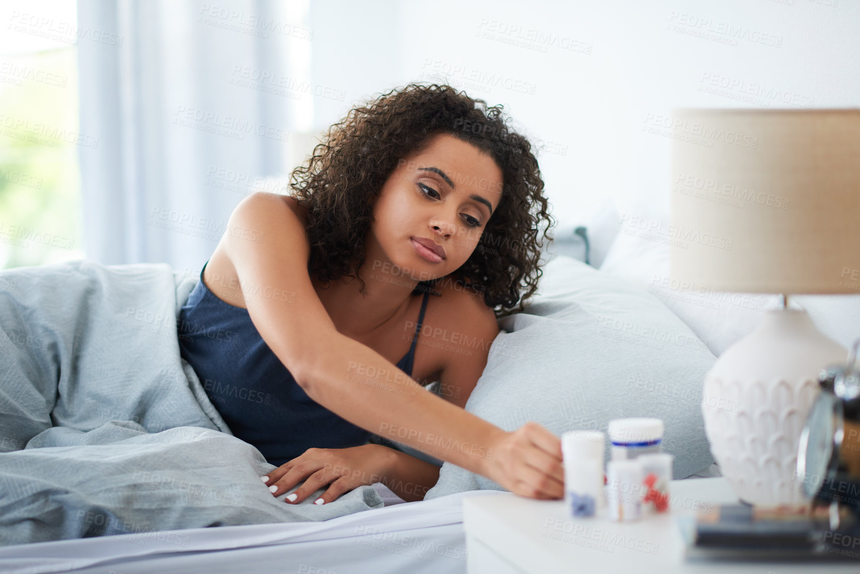 Buy stock photo Shot of an attractive young woman sitting up in bed and reaching for a container of pills in the morning