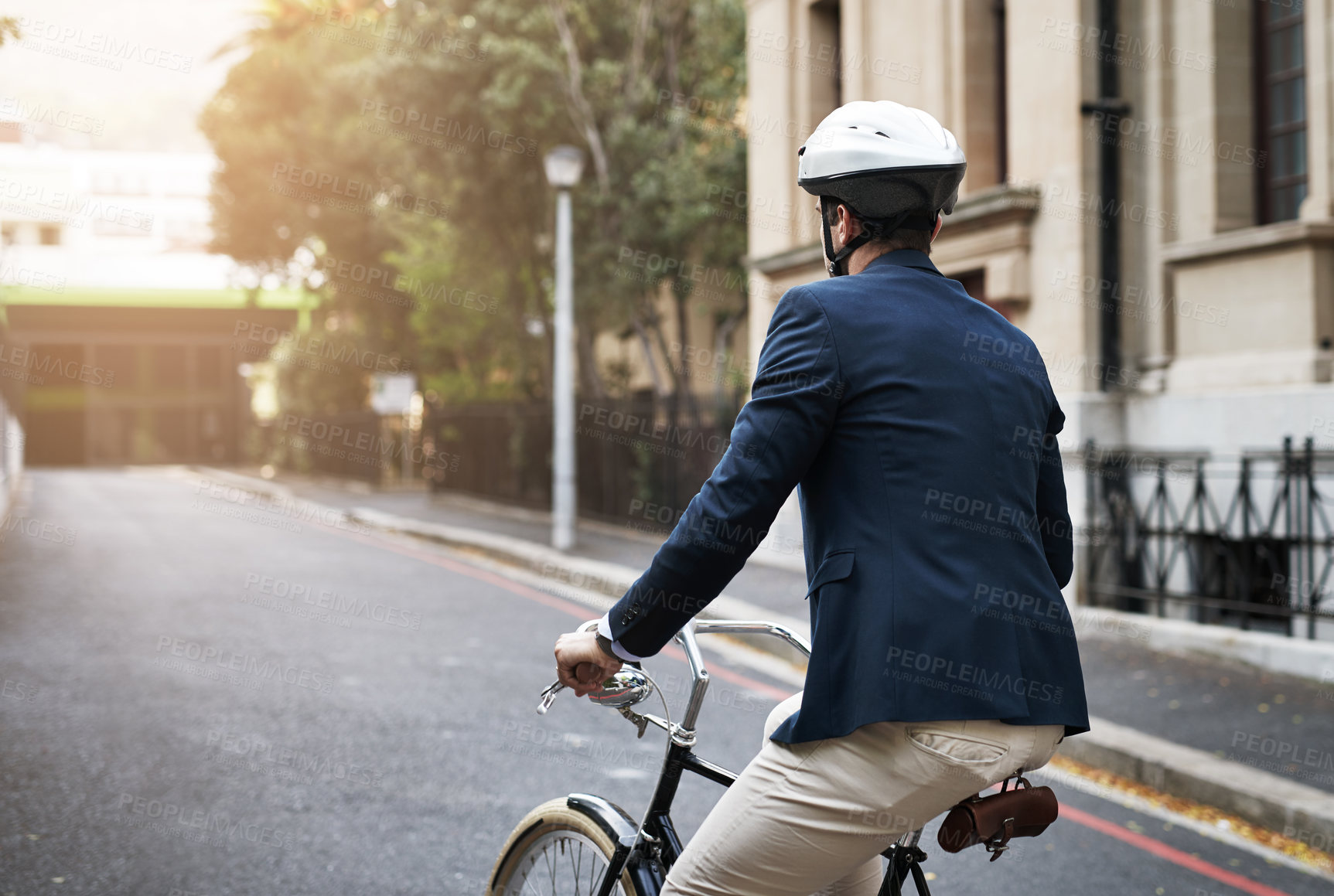 Buy stock photo Rearview shot of a handsome young businessman riding his bicycle to work in the morning