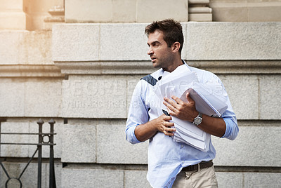 Buy stock photo Shot of a stressed out young man holding a heap of paper documents while walking to work in the morning