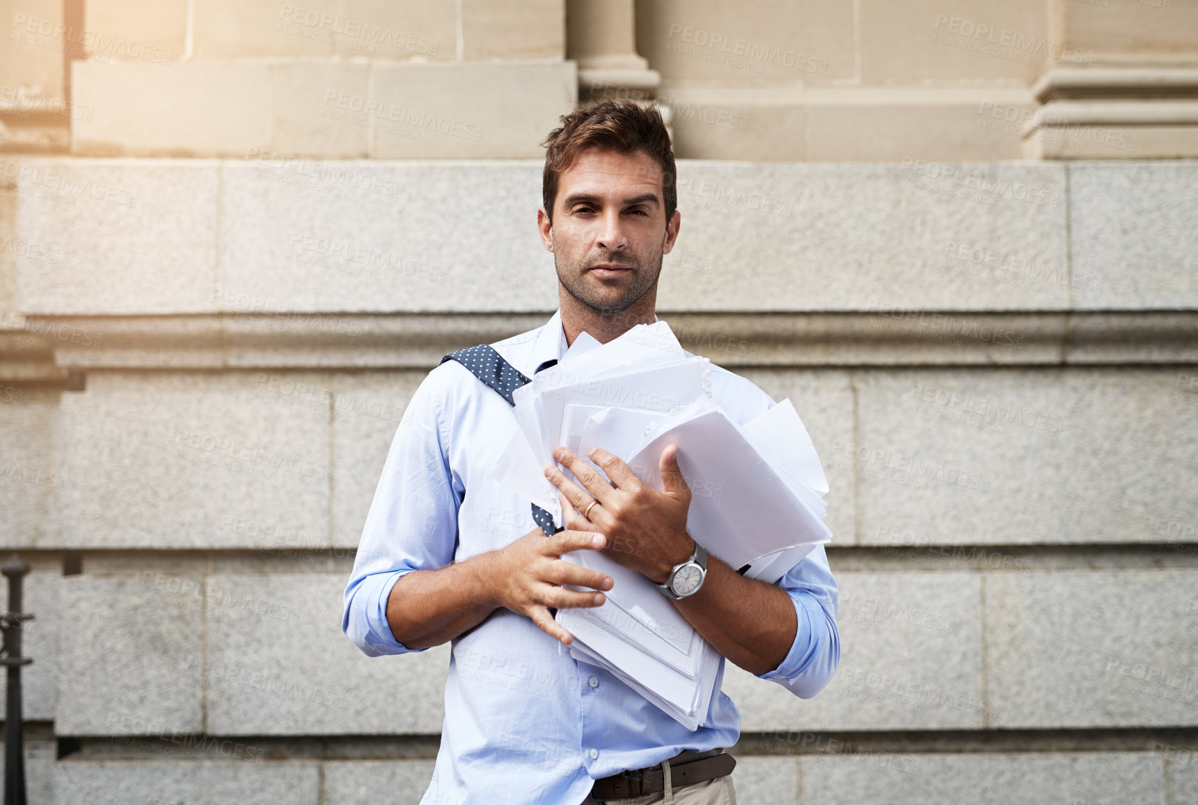 Buy stock photo Portrait of a stressed out young man holding a heap of paper documents while walking to work in the morning
