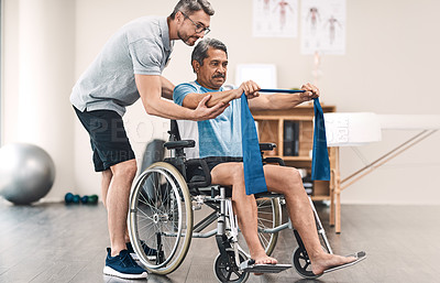 Buy stock photo Full length shot of a senior man in a wheelchair exercising with a resistance band along side his physiotherapist