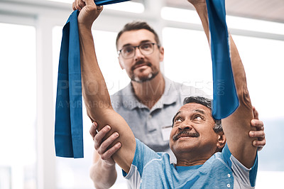 Buy stock photo Shot of a senior man exercising with a resistance band during a rehabilitation session with his physiotherapist