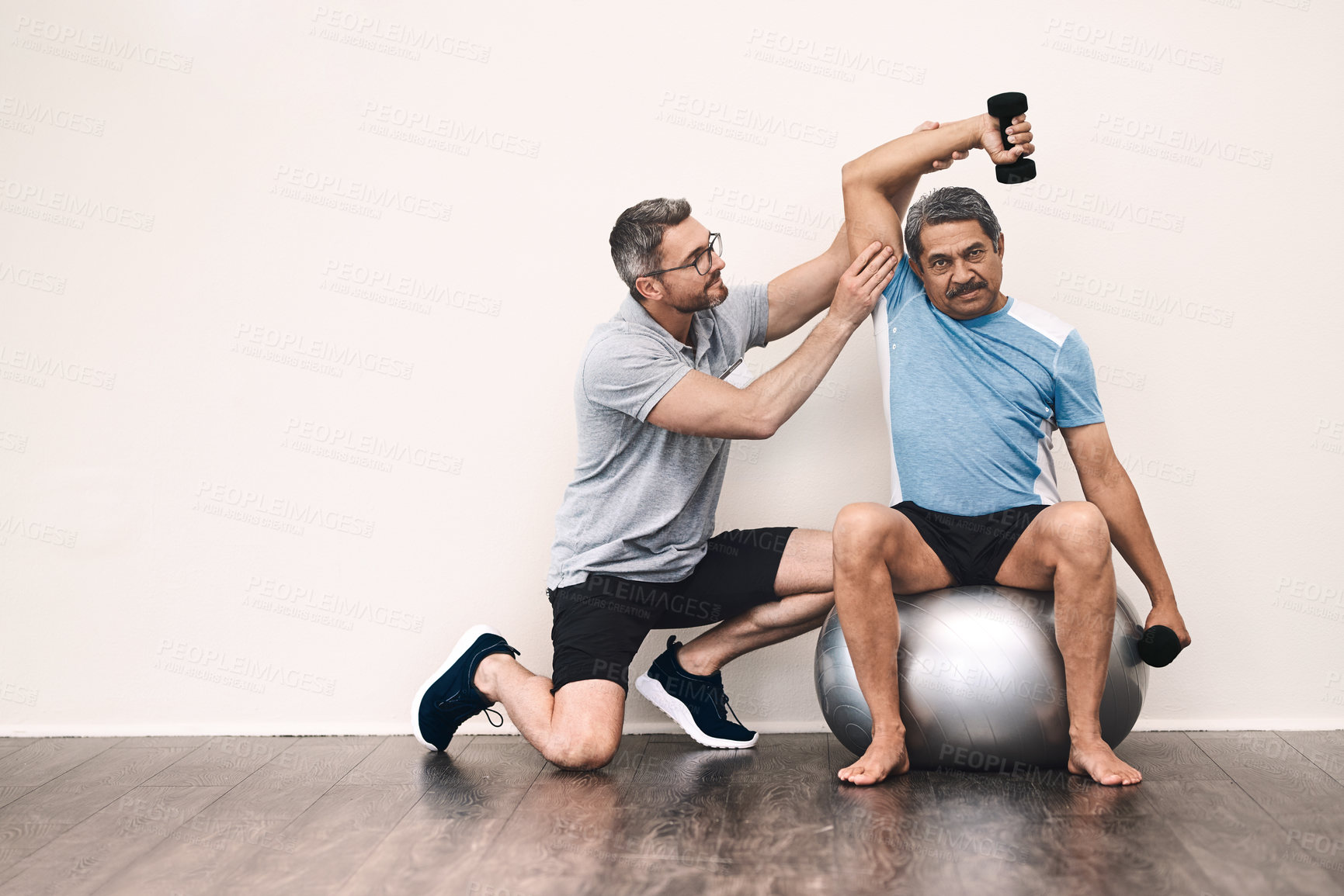 Buy stock photo Full length shot of a senior man exercising with dumbbells during a rehabilitation session with his physiotherapist