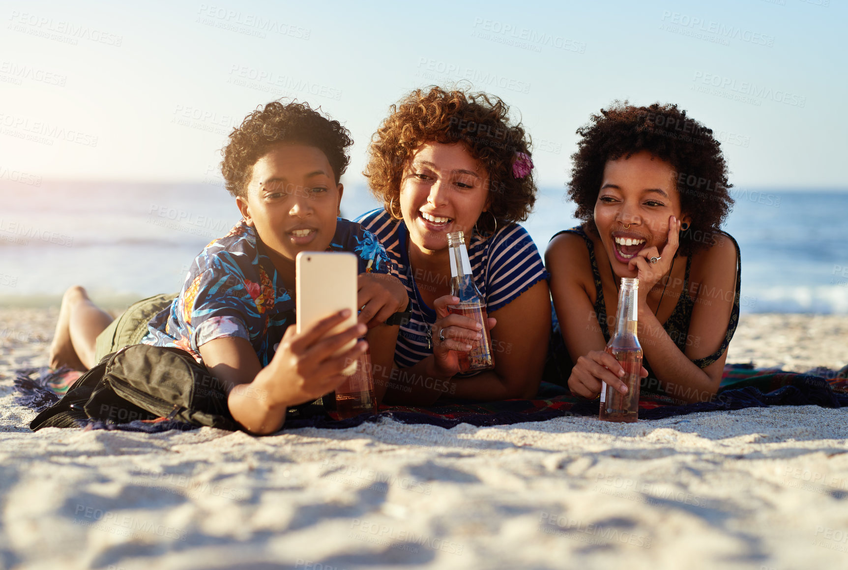Buy stock photo Shot of an attractive young trio of women laying down on the beach and taking selfies together during the day