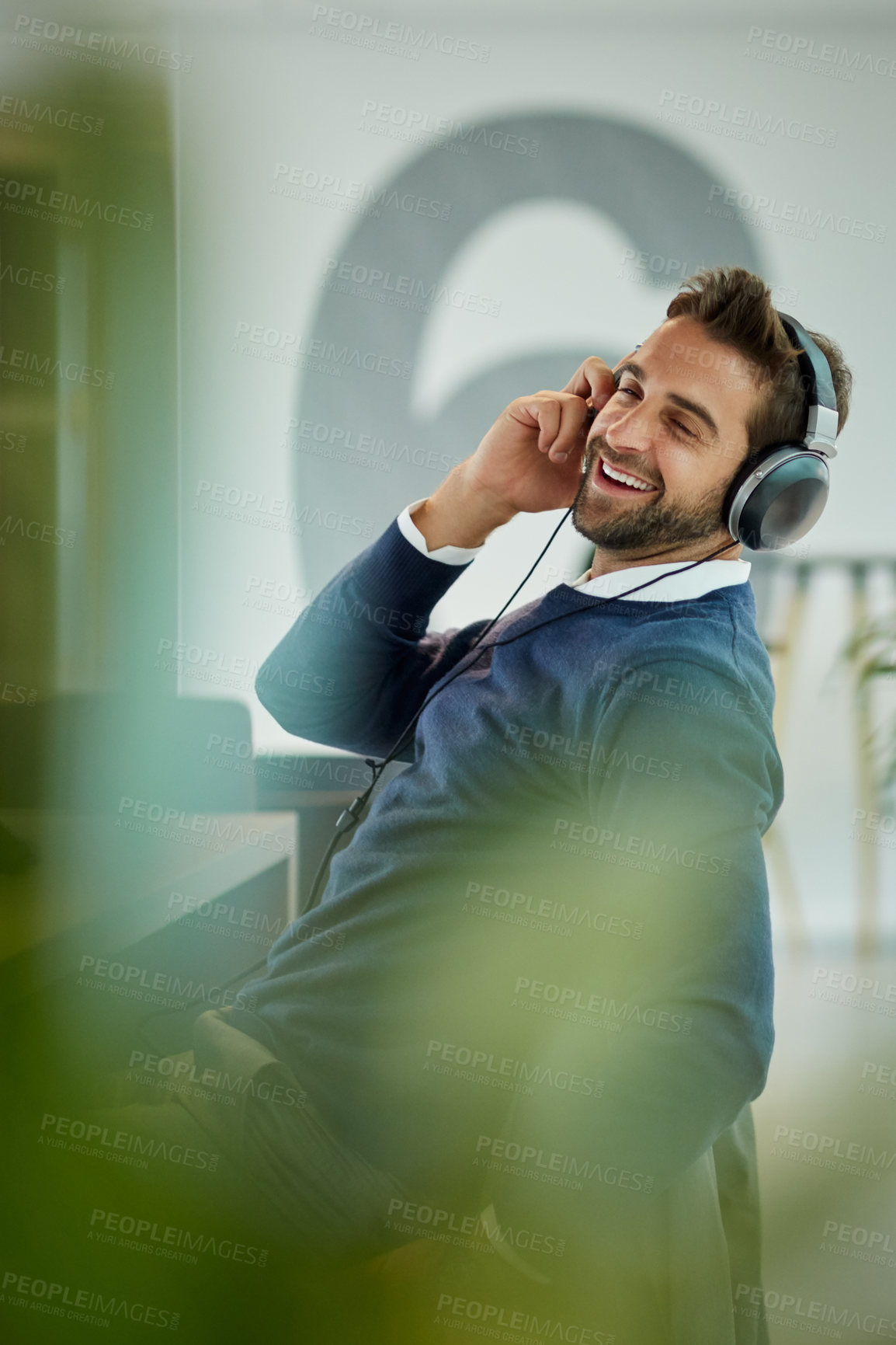 Buy stock photo Shot of a young businessman listening to music in an office