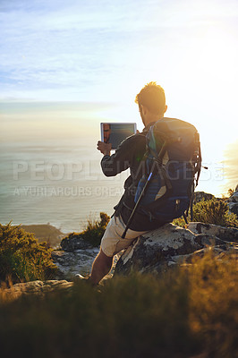 Buy stock photo Shot of a young man using a digital tablet while hiking up a mountain