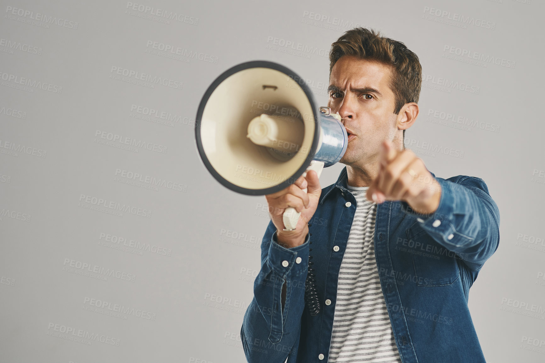 Buy stock photo Studio portrait of a young man talking into a megaphone against a grey background