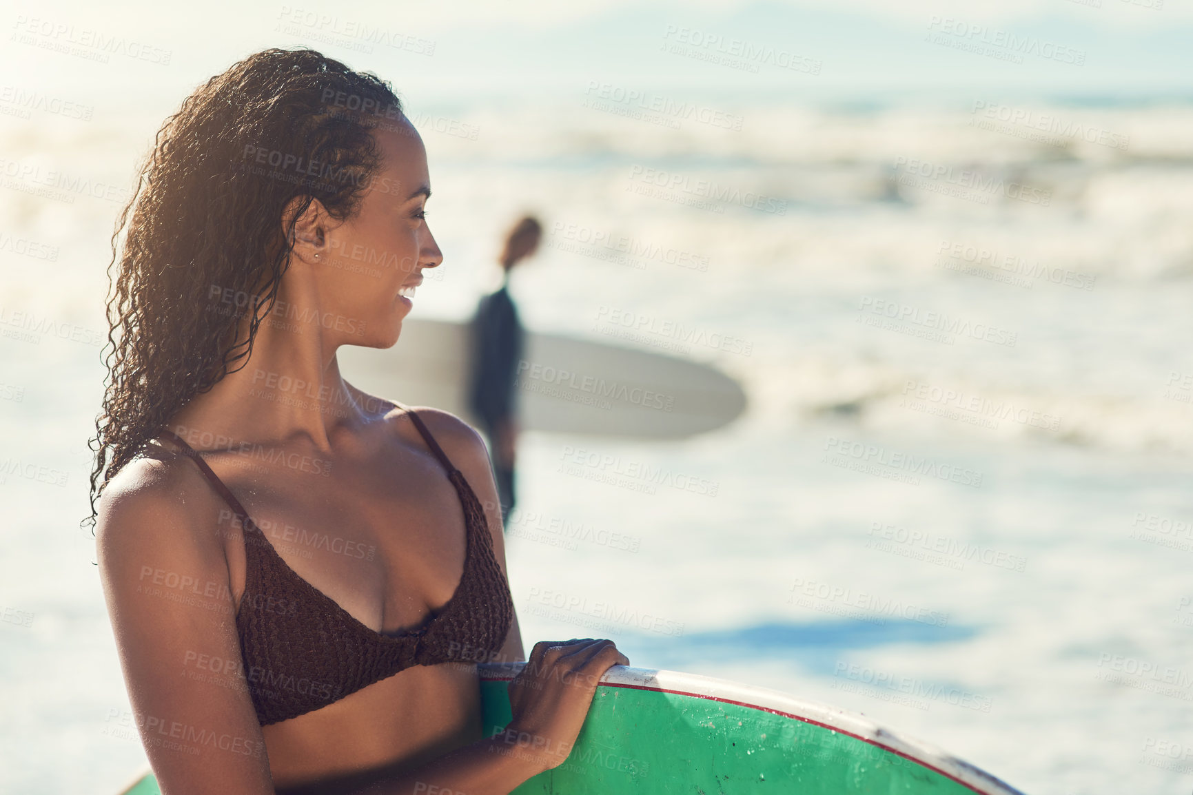 Buy stock photo Shot of a woman at the beach with her surfboard while a male surfer stands in the background