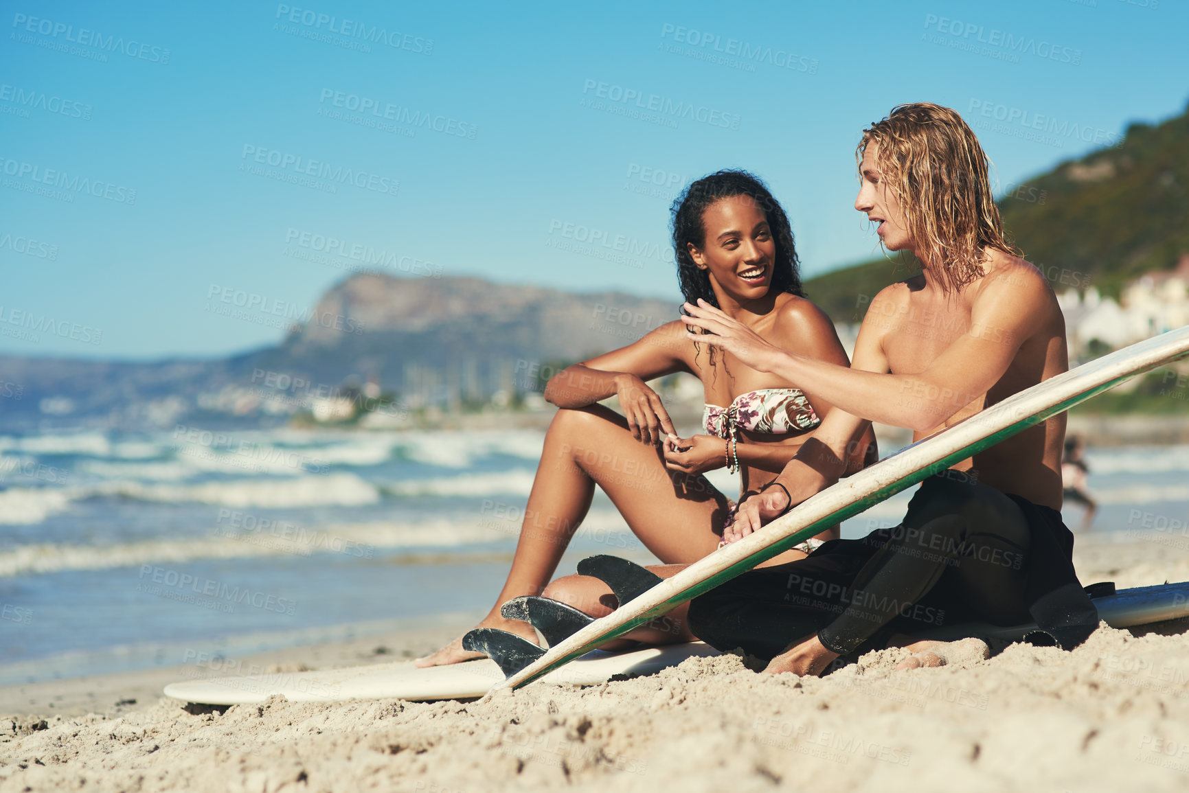 Buy stock photo Shot of a young couple sitting on the beach with their surfboards