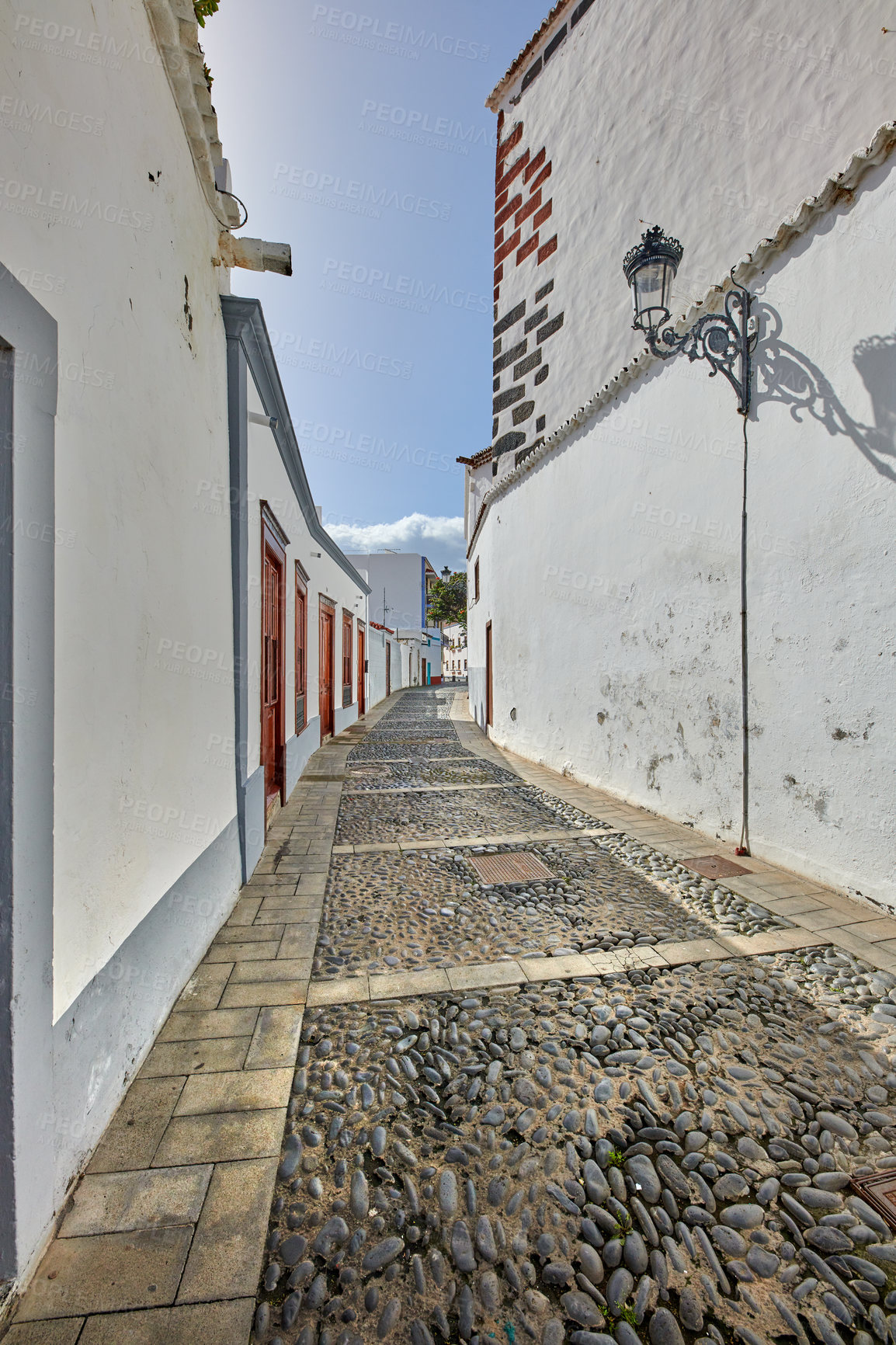 Buy stock photo Cobbled street or narrow alley between white buildings in Santa Cruz, de La Palma. Bright and vibrant classical architecture in small city or village. Beautiful houses or homes with a vintage design