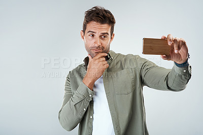 Buy stock photo Studio shot of a cheerful young man taking a self portrait with his cellphone while standing against a grey background