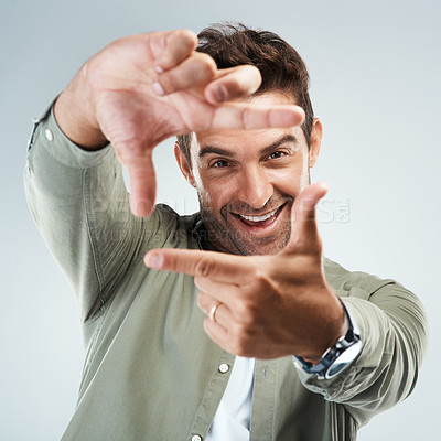 Buy stock photo Portrait of a cheerful young man making frames with his hands to simulate the angle of a camera while standing against a grey background