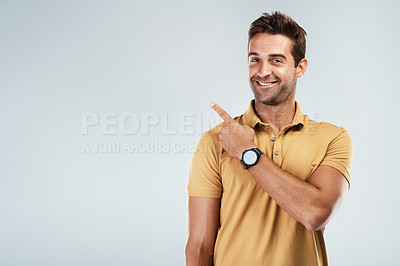 Buy stock photo Portrait of a cheerful young man pointing with his finger behind hime while standing against a grey background