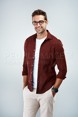 Buy stock photo Portrait of a cheerful young man wearing glasses and smiling brightly while standing against a grey background