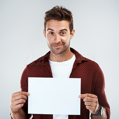 Buy stock photo Portrait of a cheerful young man holding and displaying a poster while standing against a grey background