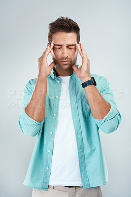 Buy stock photo Studio shot of a young man with an uncomfortable facial expression due to a headache while standing against a grey background