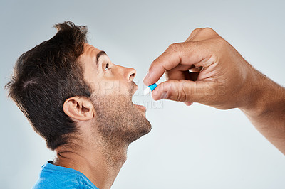 Buy stock photo Studio shot of a carefree young man receiving a pill from an unrecognizable person while standing against a grey background