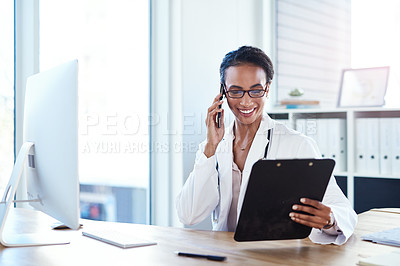 Buy stock photo Shot of a young doctor using a smartphone going over paperwork in her consulting room